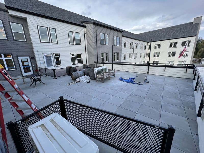 Rooftop terrace with seating and a ladder, overlooking buildings and a cloudy sky.