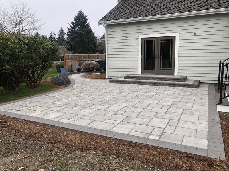 Modern patio with paver stones and landscaping, featuring a walkway and outdoor seating area.