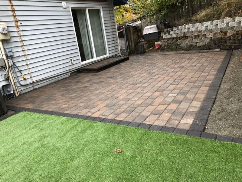 Patio area with paver stones and artificial grass beside a house. Perfect for outdoor living.