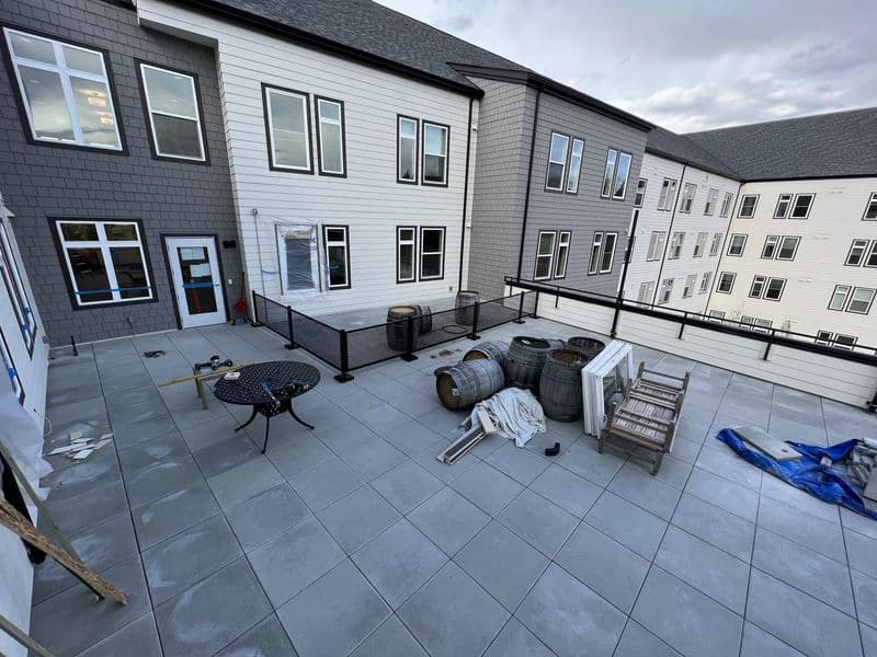 Apartment complex outdoor patio with stone tiles, furniture, and landscaping materials.