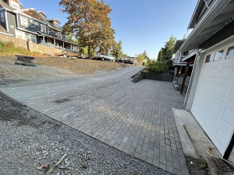Newly paved driveway with interlocking pavers, surrounded by residential homes and trees.