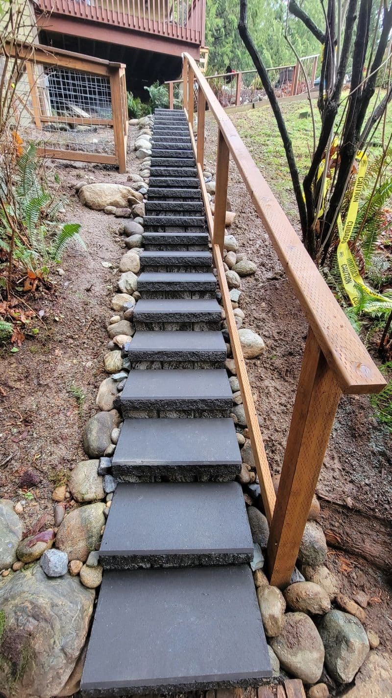 Stone steps leading up a slope with wooden railing and surrounding greenery.