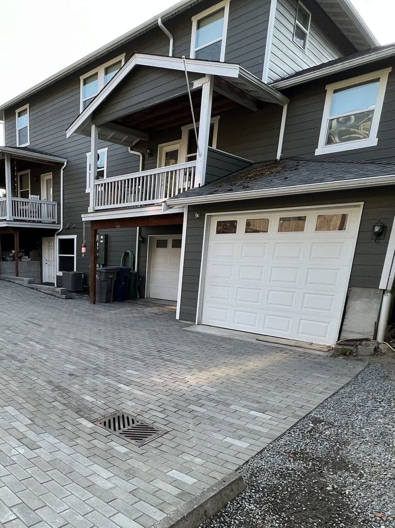 Modern two-story house with a large front porch and paved driveway. Garage to the right.
