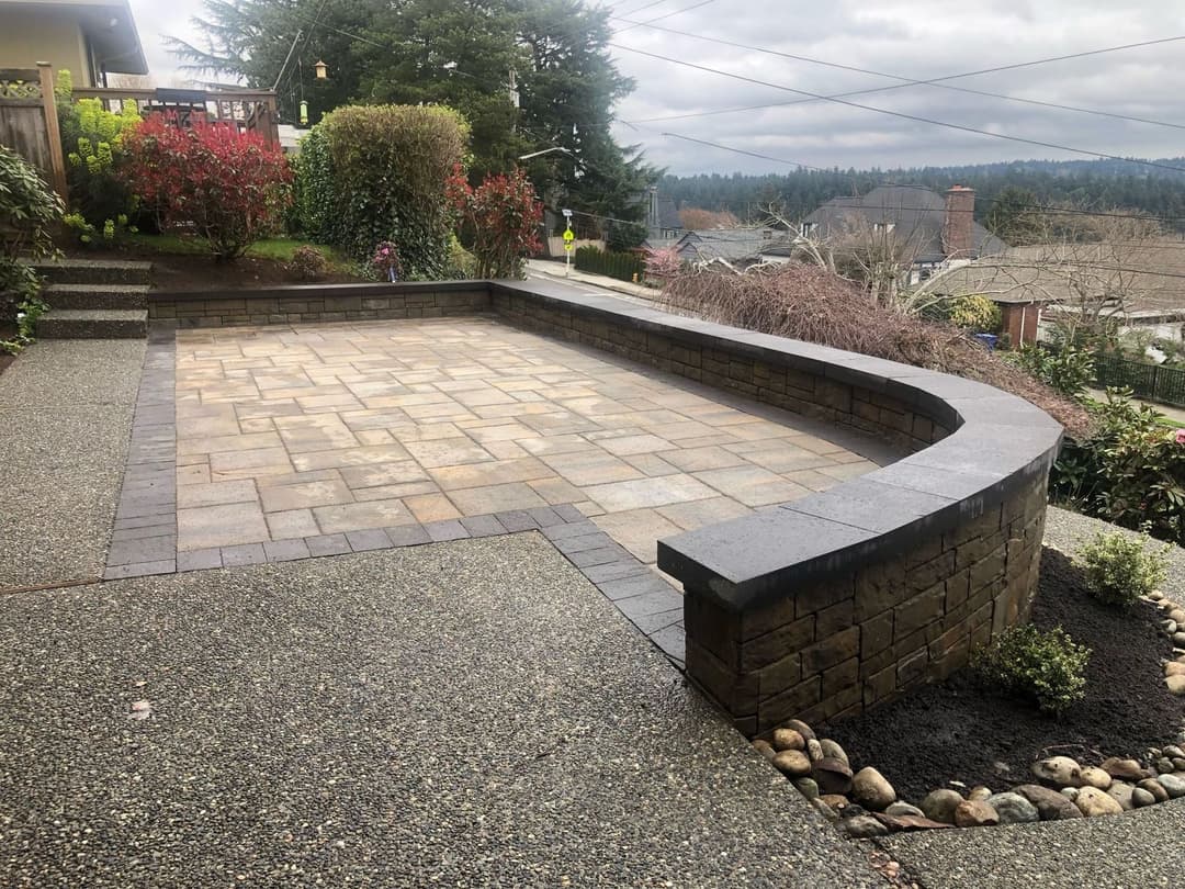 Curved stone patio with paver stones and landscaped garden in a residential backyard.