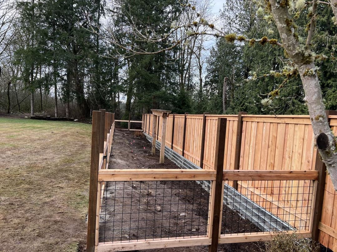Wooden fence with wire mesh in a garden, surrounded by trees and open grass area.