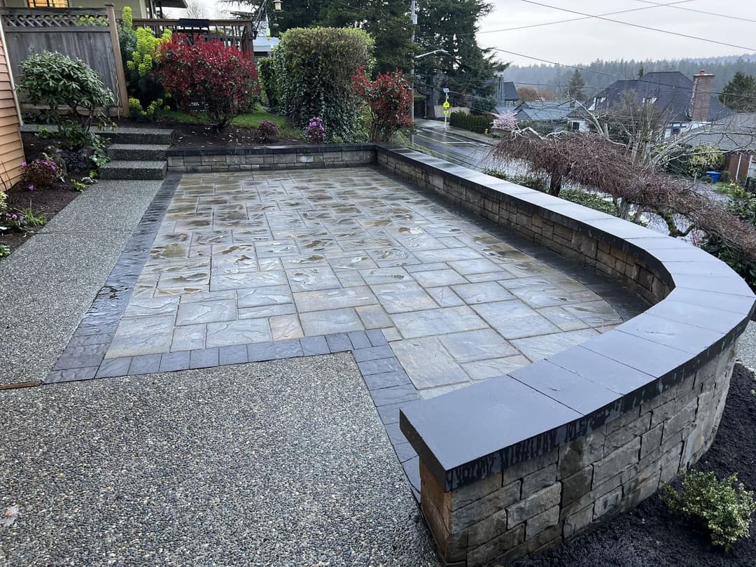 Curved patio with textured stone surface and surrounding landscape features in a residential setting.