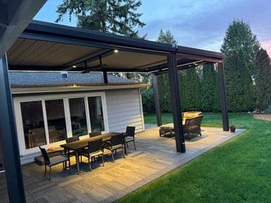 Modern backyard patio with pergola, outdoor dining area, and lush greenery at sunset.