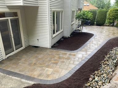 Patio area with paver stones, garden beds, and landscaping near a modern home.